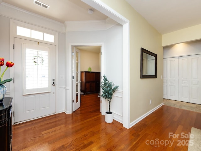 foyer featuring baseboards, visible vents, wood finished floors, and ornamental molding