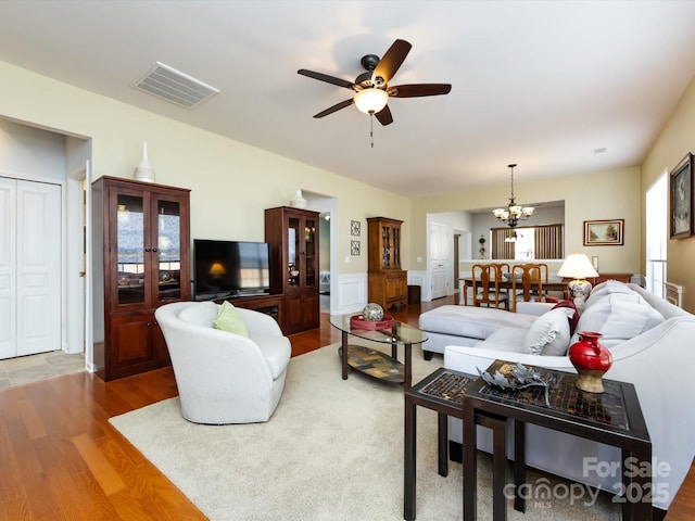 living area with visible vents, wood finished floors, and ceiling fan with notable chandelier