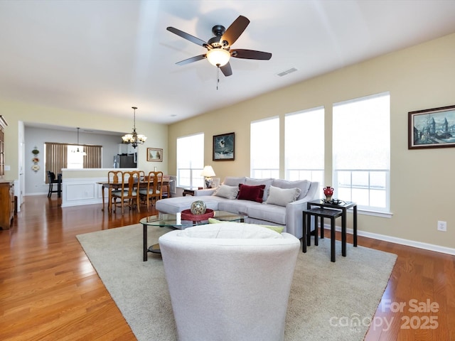 living area featuring ceiling fan with notable chandelier, wood finished floors, and baseboards