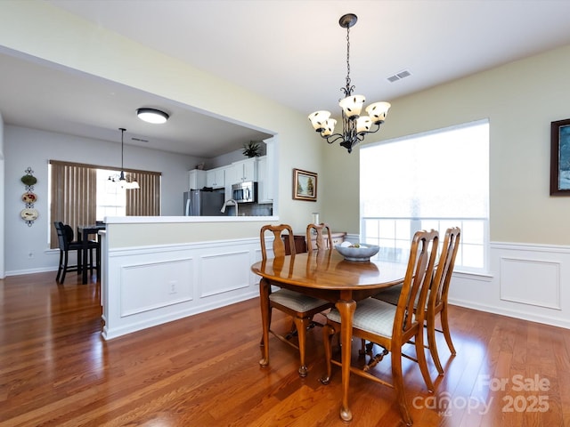 dining room with a healthy amount of sunlight, dark wood-style flooring, visible vents, and an inviting chandelier