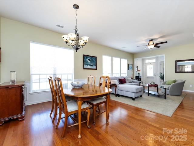 dining space with ceiling fan with notable chandelier, visible vents, baseboards, and wood finished floors