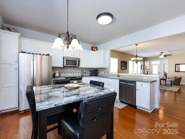 kitchen featuring stainless steel appliances, a peninsula, a sink, open floor plan, and dark wood-style floors