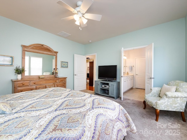 bedroom with light carpet, ensuite bath, and a ceiling fan