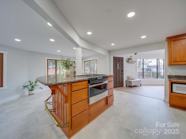 kitchen featuring gas range, dark stone counters, a breakfast bar area, and ornate columns