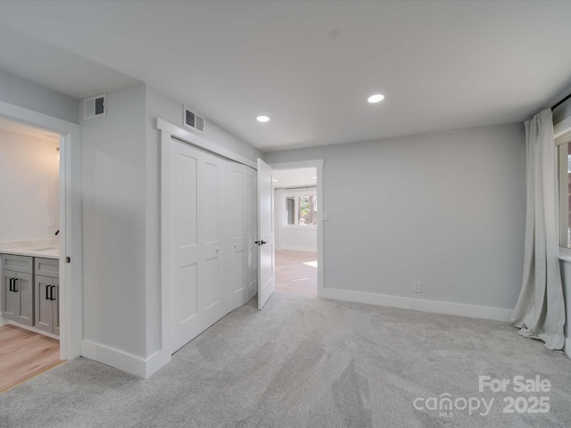 interior space featuring ensuite bath, light colored carpet, and a closet