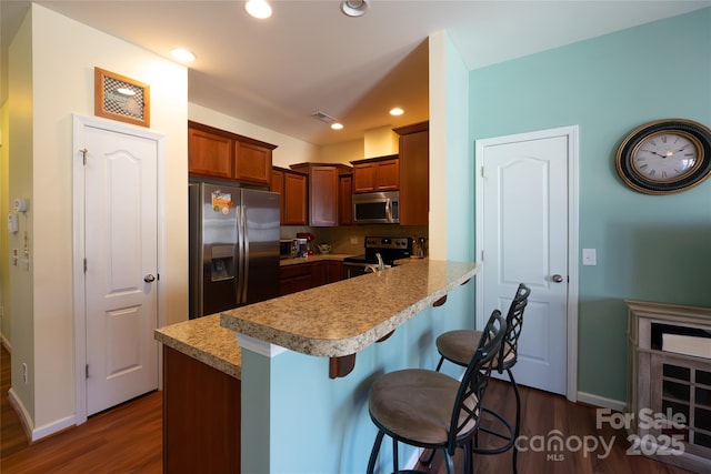 kitchen with dark hardwood / wood-style floors, appliances with stainless steel finishes, a kitchen bar, and kitchen peninsula