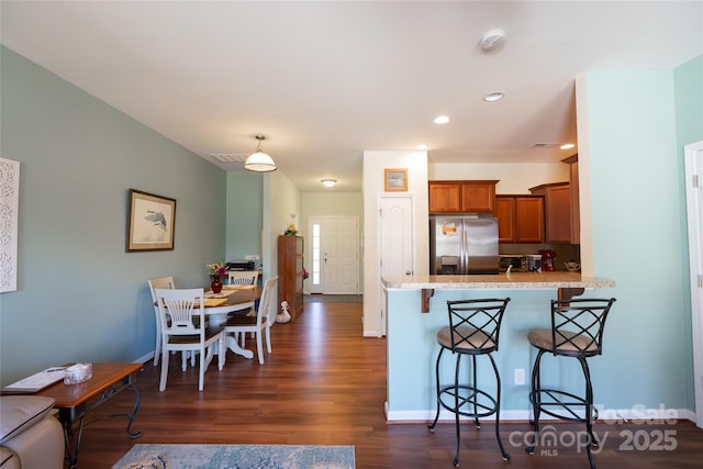 kitchen featuring dark hardwood / wood-style floors, kitchen peninsula, stainless steel fridge with ice dispenser, and a breakfast bar area