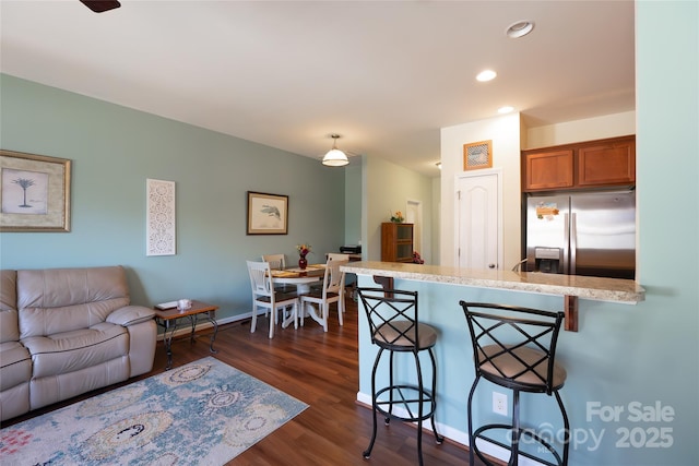 kitchen with hanging light fixtures, a kitchen bar, dark hardwood / wood-style flooring, stainless steel fridge with ice dispenser, and kitchen peninsula