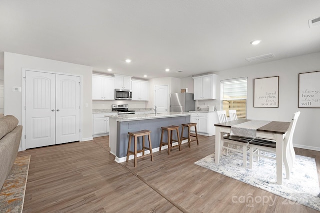 kitchen featuring a kitchen bar, wood-type flooring, stainless steel appliances, a kitchen island with sink, and white cabinets