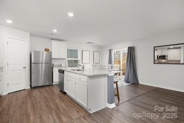 kitchen with an island with sink, sink, white cabinets, dark hardwood / wood-style flooring, and stainless steel appliances