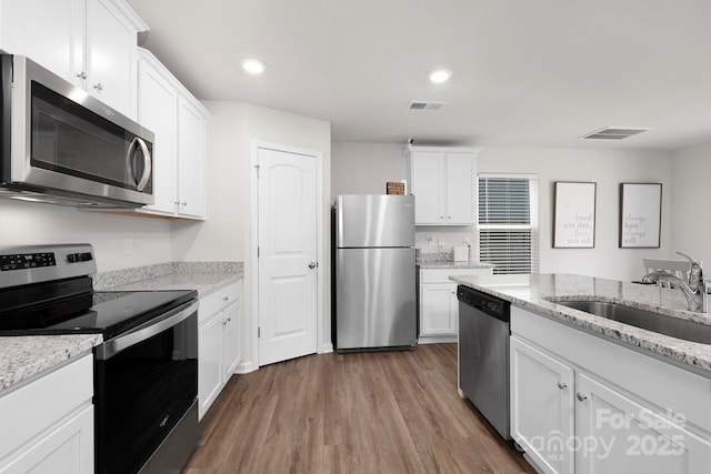 kitchen with light stone counters, stainless steel appliances, sink, and white cabinets