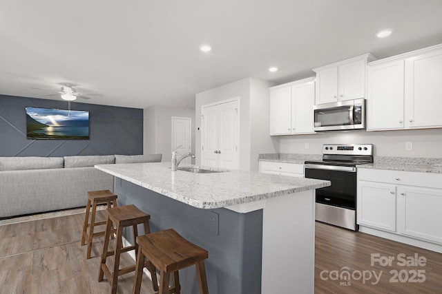 kitchen with white cabinetry, stainless steel appliances, sink, and a center island with sink