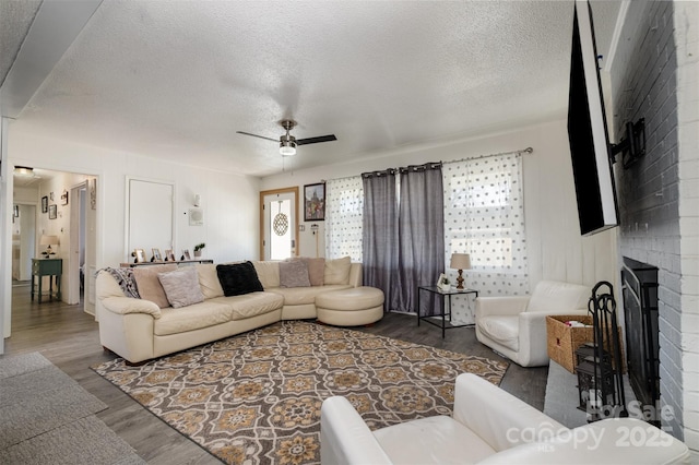 living room featuring ceiling fan, a brick fireplace, dark wood-type flooring, and a textured ceiling