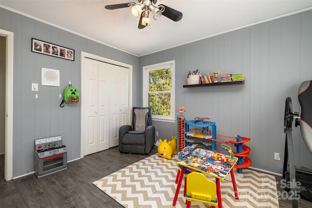 game room with dark wood-type flooring, ceiling fan, ornamental molding, and a textured ceiling