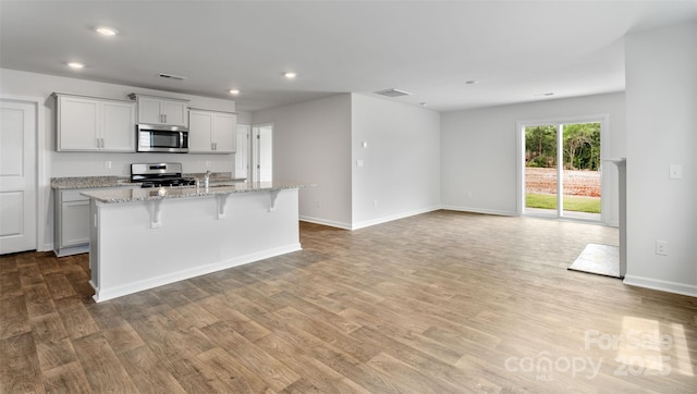 kitchen with a breakfast bar, appliances with stainless steel finishes, light stone counters, an island with sink, and light wood-type flooring