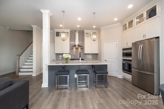 kitchen with white cabinetry, wall chimney range hood, stainless steel appliances, and hanging light fixtures