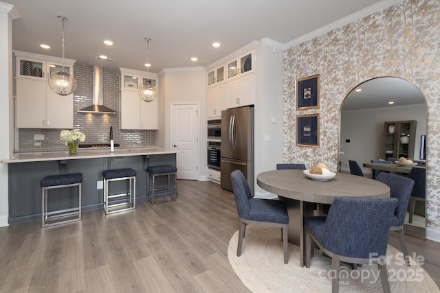 kitchen with wall chimney exhaust hood, white cabinetry, stainless steel refrigerator, pendant lighting, and light hardwood / wood-style floors