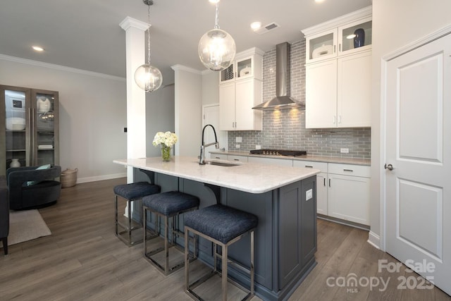 kitchen with white cabinetry, sink, wall chimney range hood, and a kitchen island with sink