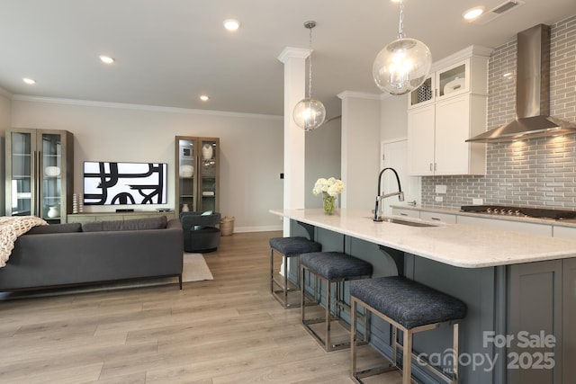 kitchen with white cabinetry, sink, an island with sink, and wall chimney exhaust hood