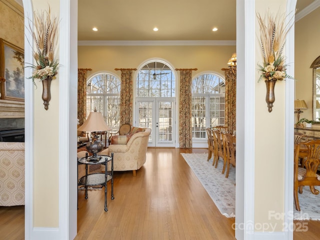 living area with ornamental molding, a wealth of natural light, light wood-type flooring, and french doors