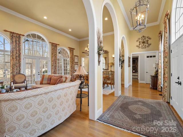 foyer entrance featuring french doors, crown molding, a chandelier, light wood-type flooring, and a high ceiling