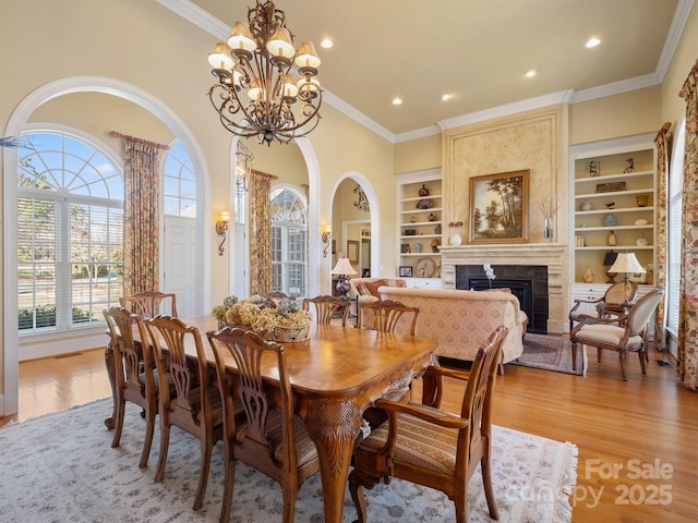 dining area featuring crown molding, a large fireplace, light hardwood / wood-style floors, and built in features