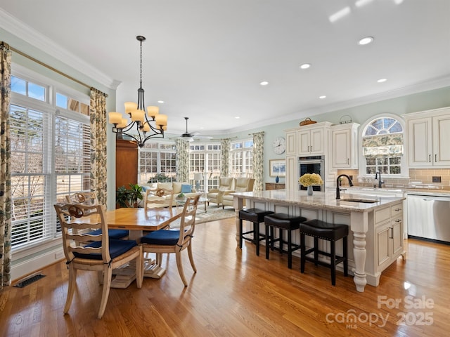 dining area with ornamental molding, sink, light hardwood / wood-style flooring, and a notable chandelier