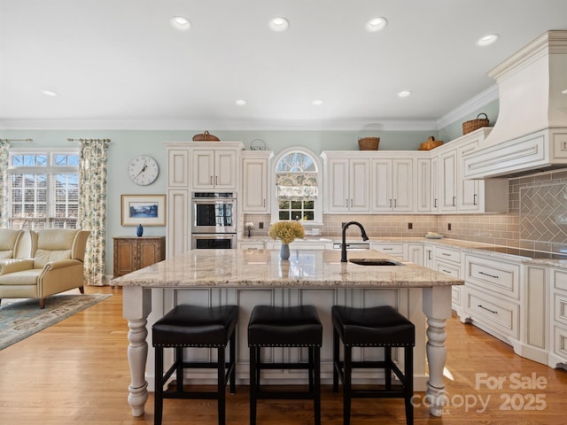 kitchen with sink, a breakfast bar area, light stone countertops, a center island with sink, and custom exhaust hood