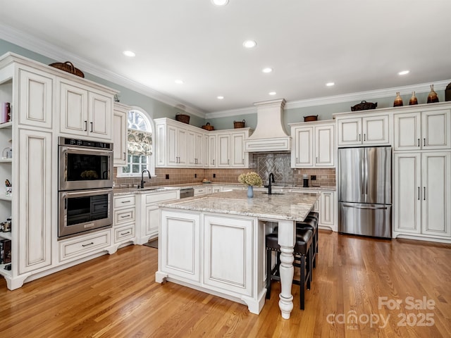 kitchen with appliances with stainless steel finishes, a breakfast bar, sink, custom range hood, and a center island with sink