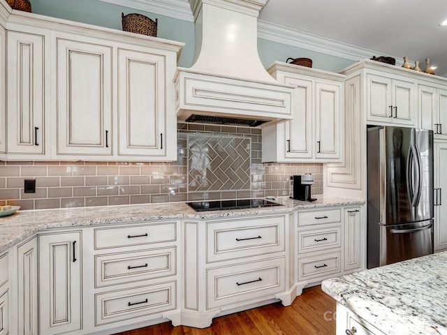 kitchen with ornamental molding, custom range hood, light stone counters, and stainless steel refrigerator