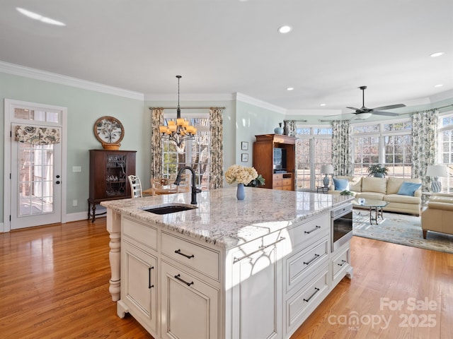 kitchen featuring pendant lighting, sink, light stone counters, a center island with sink, and light wood-type flooring