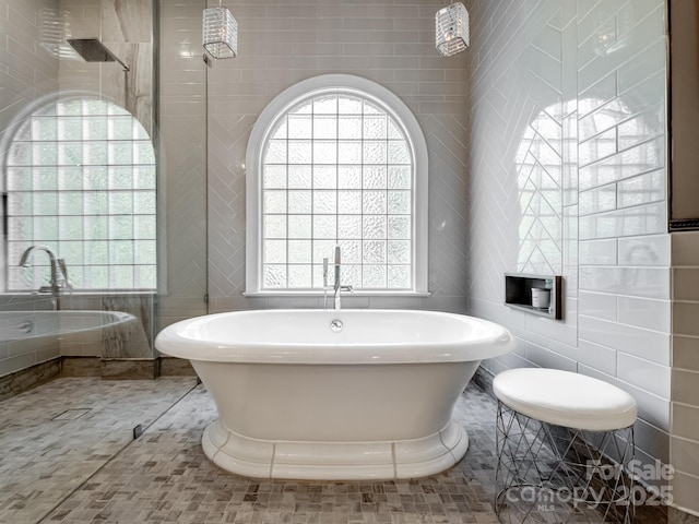 bathroom with tile patterned floors, a healthy amount of sunlight, a bathtub, and tile walls