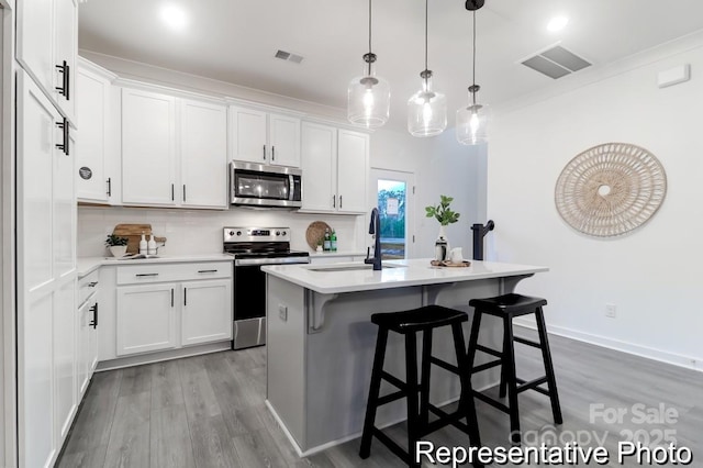 kitchen with appliances with stainless steel finishes, a kitchen island with sink, sink, and white cabinets