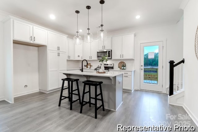 kitchen featuring pendant lighting, white cabinetry, stainless steel appliances, and a center island with sink