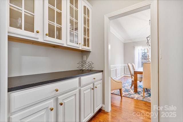 bar featuring white cabinetry, crown molding, and light hardwood / wood-style flooring