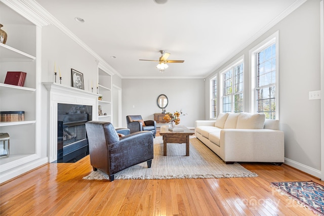 living room with crown molding, built in features, ceiling fan, and light hardwood / wood-style flooring