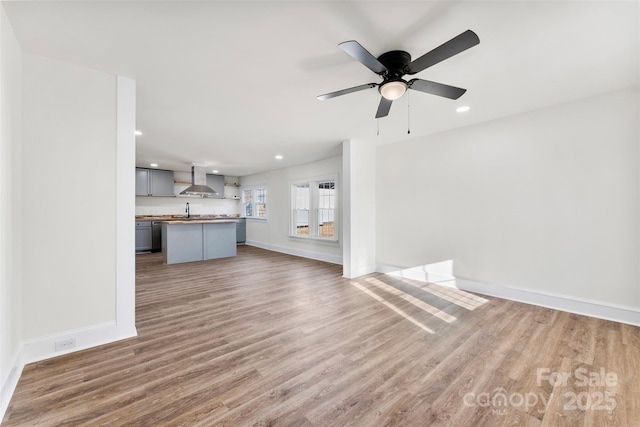 unfurnished living room featuring hardwood / wood-style floors, sink, and ceiling fan