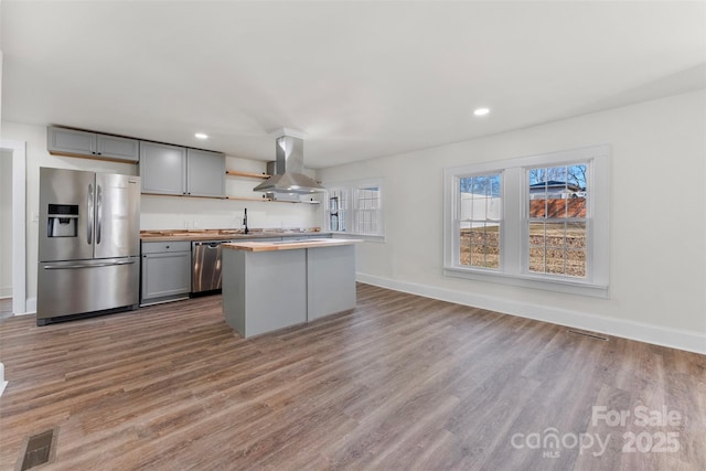 kitchen with appliances with stainless steel finishes, gray cabinetry, hardwood / wood-style floors, island exhaust hood, and a kitchen island