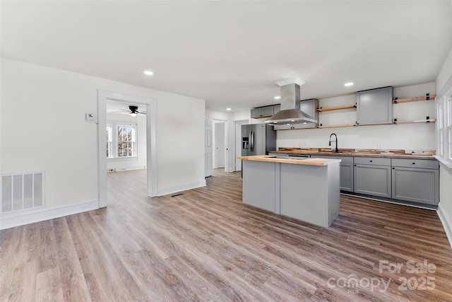 kitchen with gray cabinets, island range hood, wood-type flooring, wooden counters, and stainless steel fridge with ice dispenser