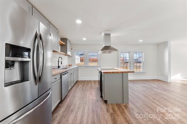 kitchen with wood counters, sink, gray cabinetry, island exhaust hood, and stainless steel appliances