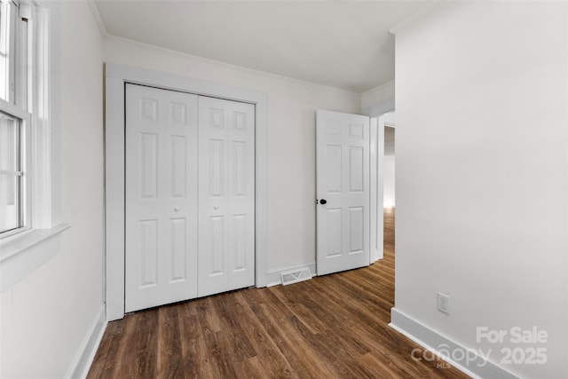 unfurnished bedroom featuring multiple windows, crown molding, dark hardwood / wood-style flooring, and a closet