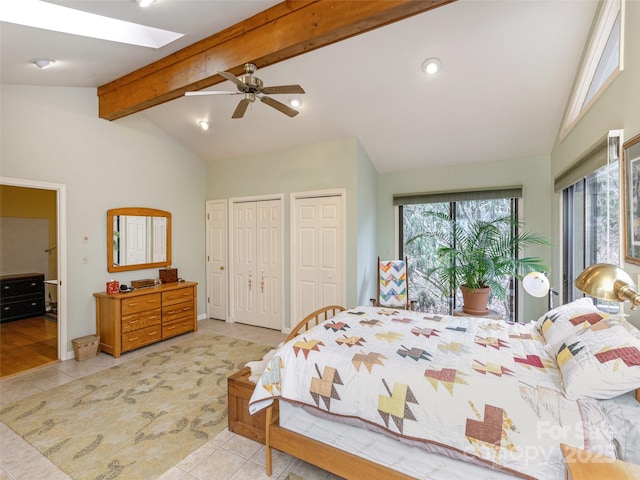 tiled bedroom featuring ceiling fan, vaulted ceiling with skylight, and two closets