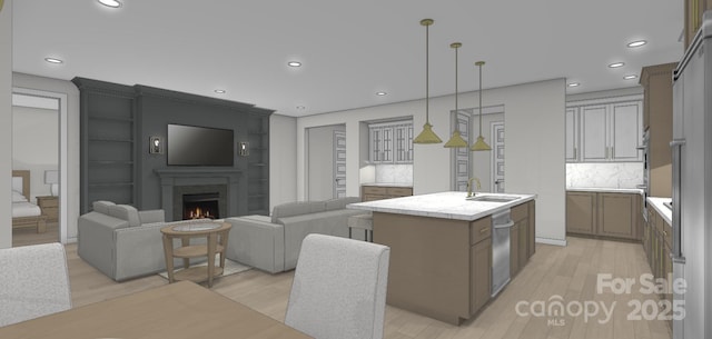 kitchen with a warm lit fireplace, light countertops, an island with sink, a sink, and light wood-type flooring