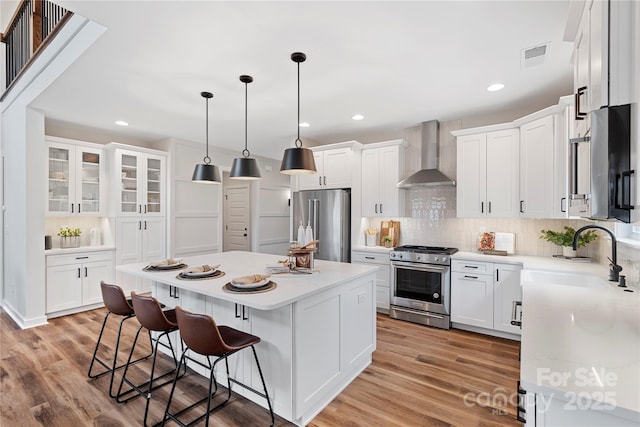 kitchen with high quality appliances, white cabinetry, a center island, and wall chimney exhaust hood