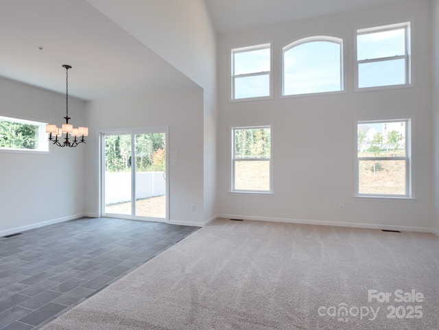 unfurnished living room with an inviting chandelier, a towering ceiling, and dark carpet