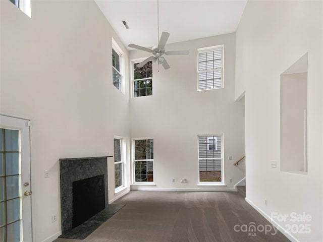 unfurnished living room featuring ceiling fan, a towering ceiling, a premium fireplace, and dark colored carpet