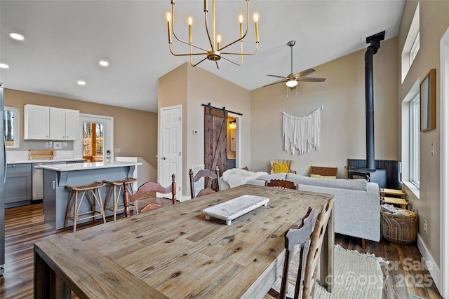 dining room with dark hardwood / wood-style floors, ceiling fan, a barn door, and a wood stove