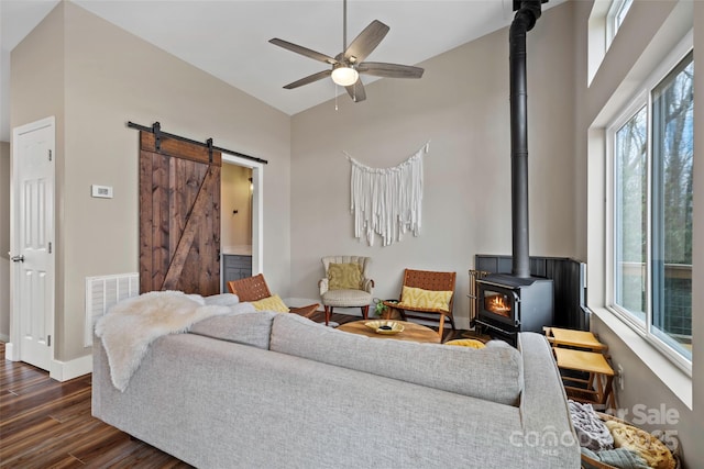 living room featuring ceiling fan, a towering ceiling, dark hardwood / wood-style flooring, a barn door, and a wood stove