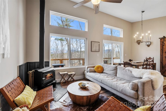 living room featuring hardwood / wood-style floors, a high ceiling, a wood stove, and ceiling fan with notable chandelier