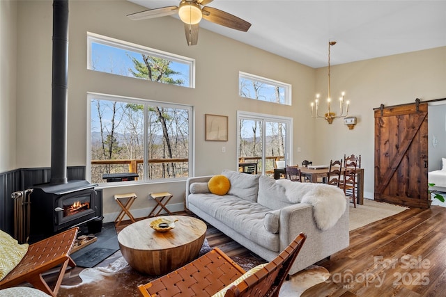 living area with a barn door, a towering ceiling, wood finished floors, a wood stove, and ceiling fan with notable chandelier